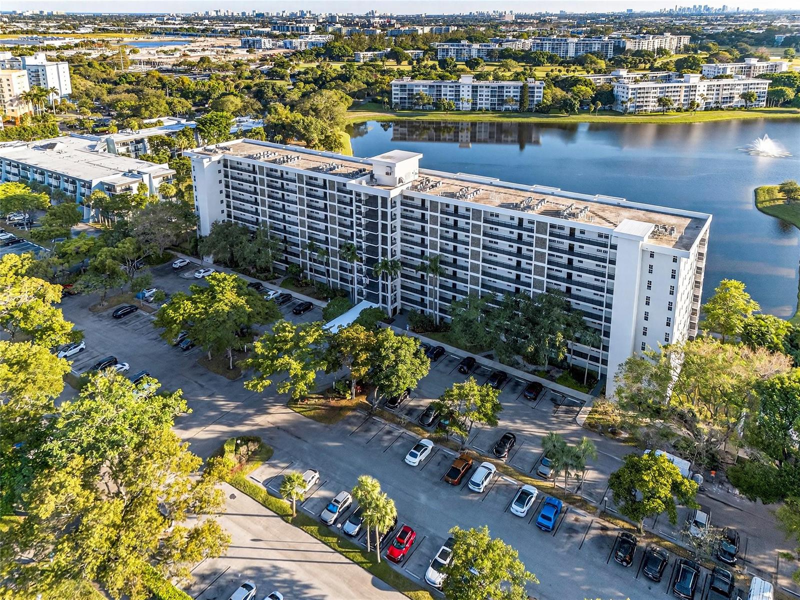 An aerial view shows a multi-story apartment building next to a lake and parking lot — 2900 N Course Drive # 607, Pompano Beach FL 33069, POMPANO BEACH, FL