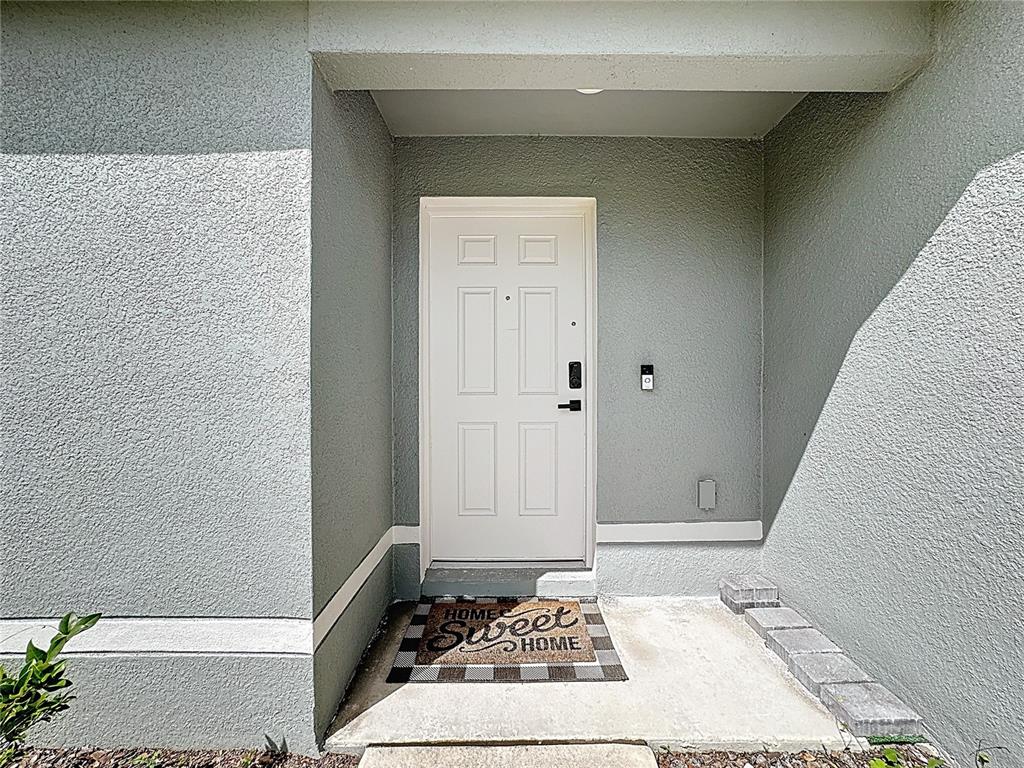 A white front door with a welcome mat is set within a gray stucco entryway — 120 BONITO WAY, KISSIMMEE, FL