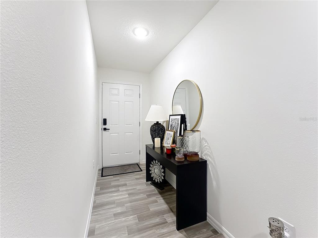 An entryway features a black console table, a round mirror, and light wood-look flooring — 120 BONITO WAY, KISSIMMEE, FL