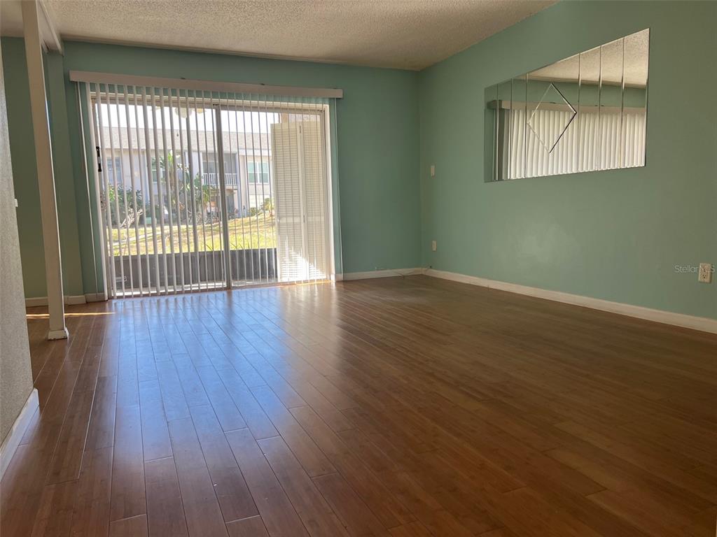 An empty living room features light green walls, wood-look flooring, and a sliding glass door — 2625 STATE ROAD 590 UNIT 2514, CLEARWATER, FL