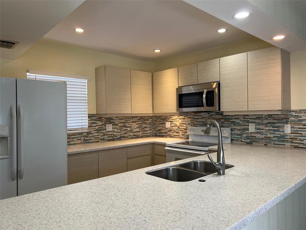 A kitchen features light wood cabinets, a speckled countertop, and a multi-colored glass tile backsplash — 2625 STATE ROAD 590 UNIT 2514, CLEARWATER, FL