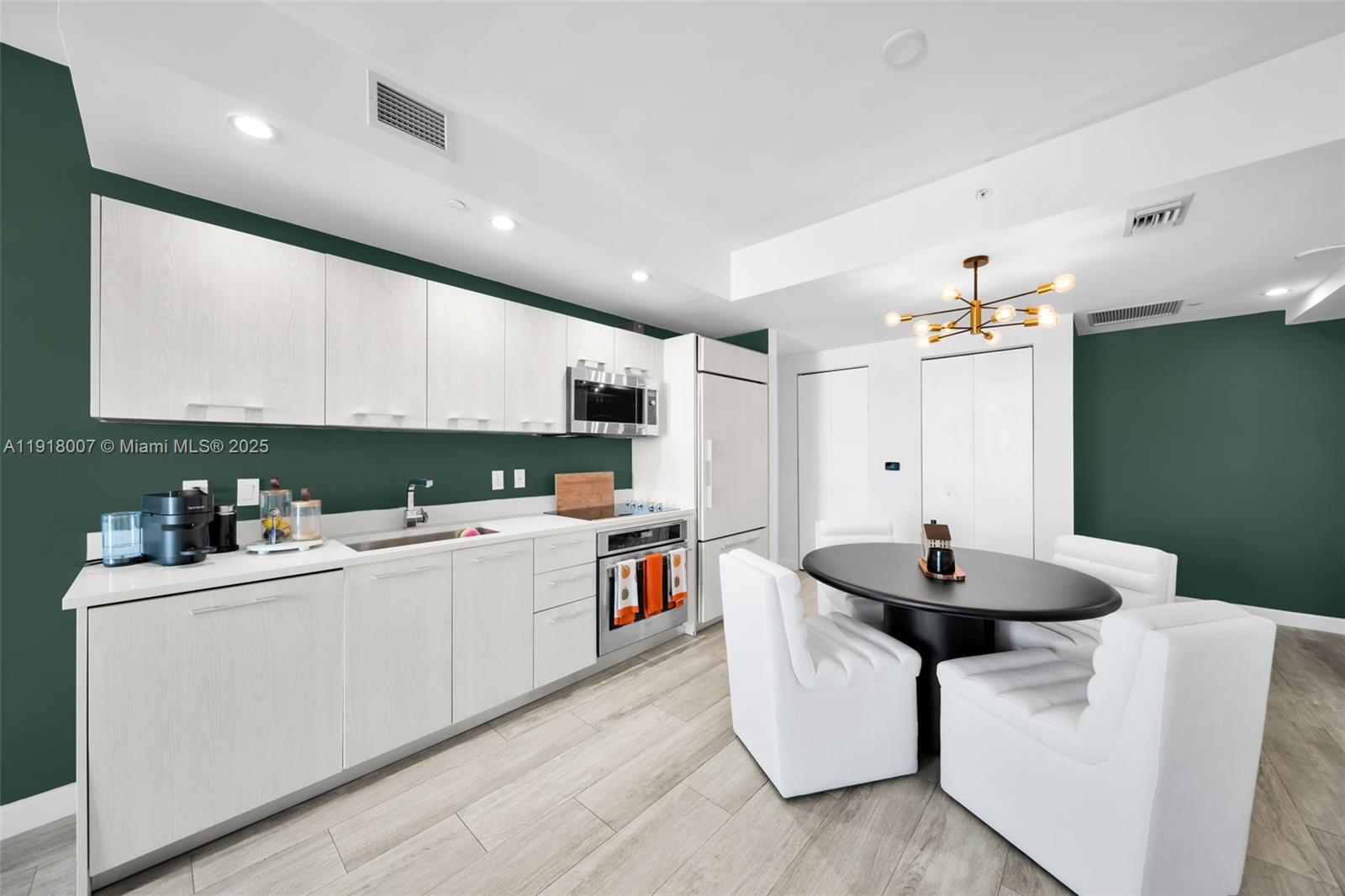 A modern kitchen features white cabinetry, a dark green accent wall, and a dining area — 45 SW 9th St # 3909, Miami FL 33130, MIAMI, FL