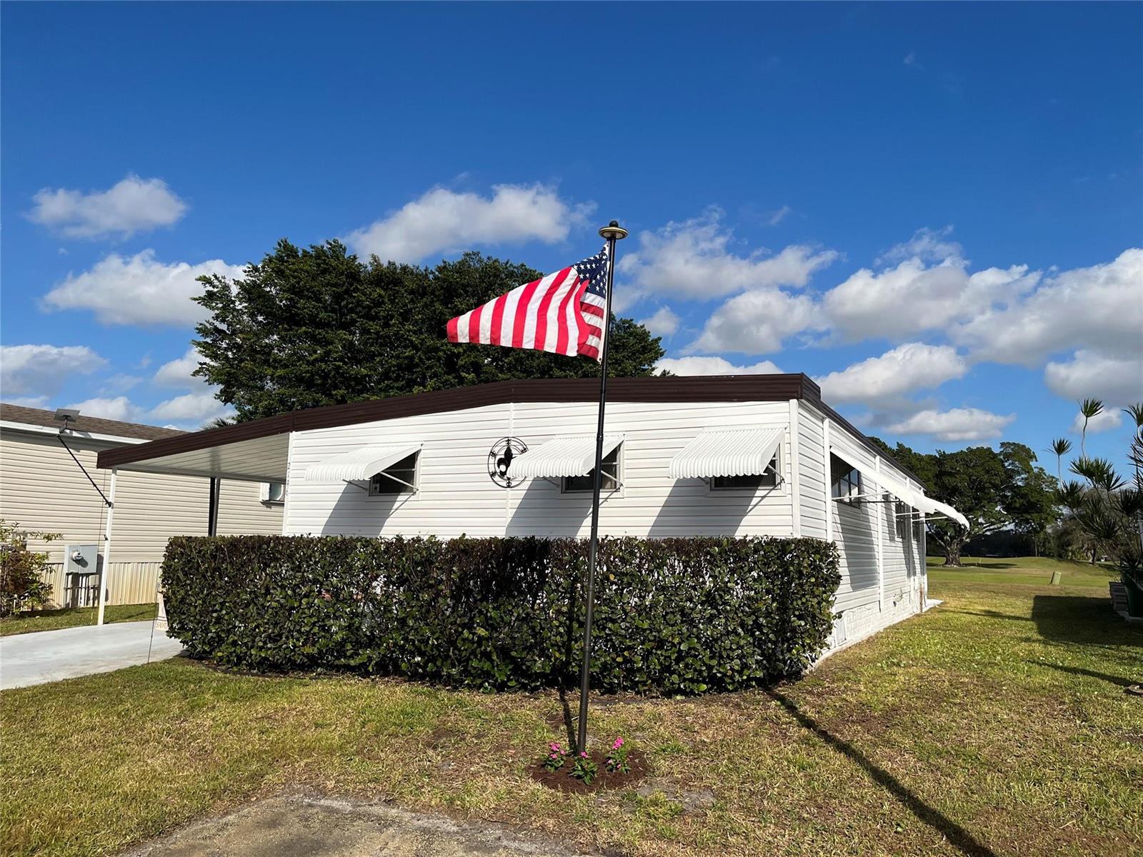A white mobile home with a flag pole and hedge sits under a blue sky — 2196 SW 83rd Avenue, Davie FL 33324, DAVIE, FL