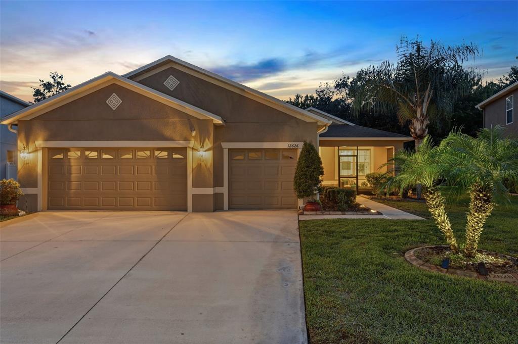 A single-story house with a two-car garage and a landscaped front yard at dusk — 12626 JILLIAN CIRCLE, HUDSON, FL