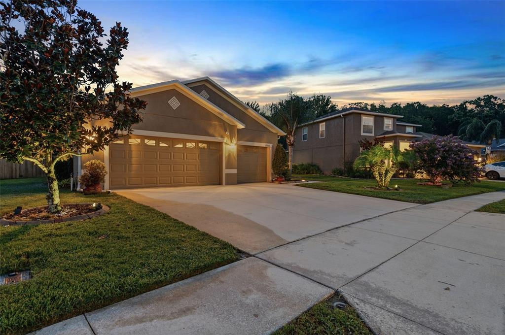 A tan suburban house with a three-car garage and a concrete driveway at dusk — 12626 JILLIAN CIRCLE, HUDSON, FL