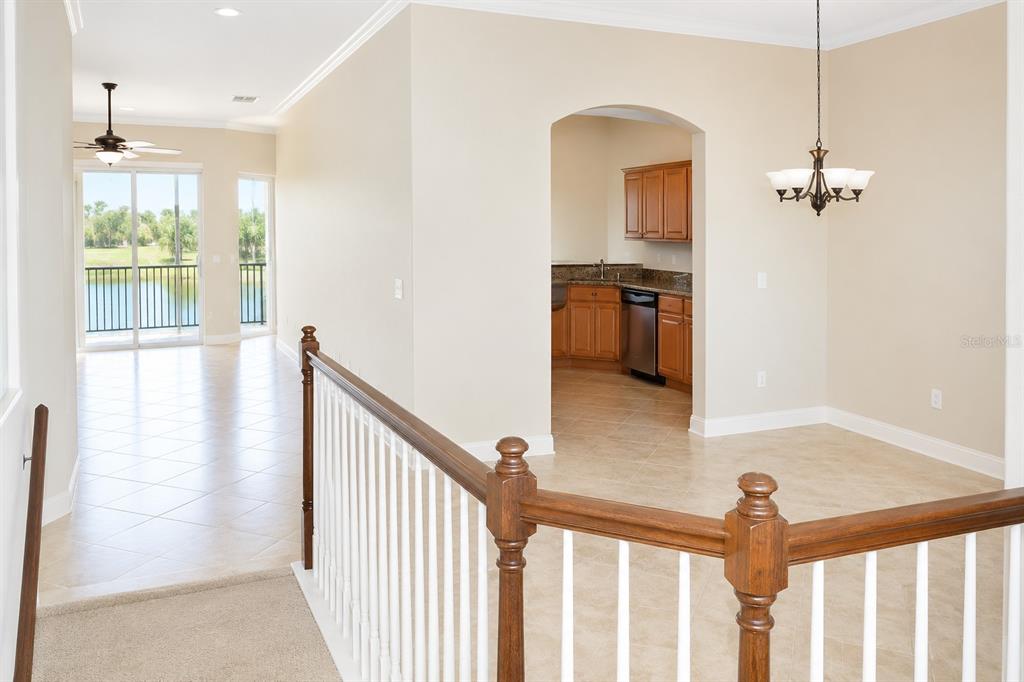 An interior view shows a carpeted staircase landing leading to a tiled dining area and kitchen — 8361 MIRAMAR WAY, LAKEWOOD RANCH, FL