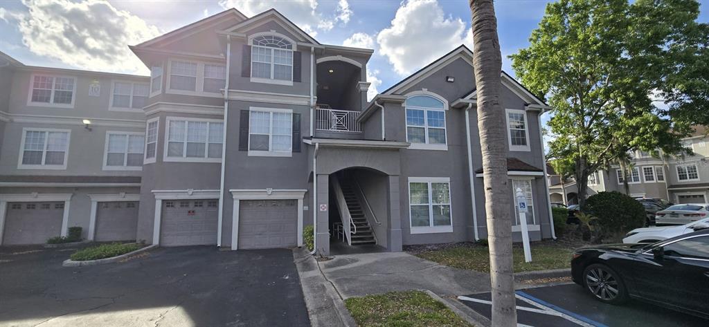A multi-story gray apartment building features ground-level garages, an exterior staircase, and a parking lot — 3379 S KIRKMAN ROAD UNIT 1015, ORLANDO, FL
