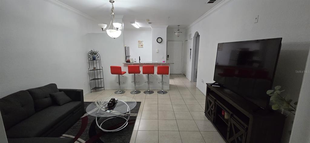 A living room with a dark sofa, glass coffee table, and a breakfast bar with stools — 3379 S KIRKMAN ROAD UNIT 1015, ORLANDO, FL