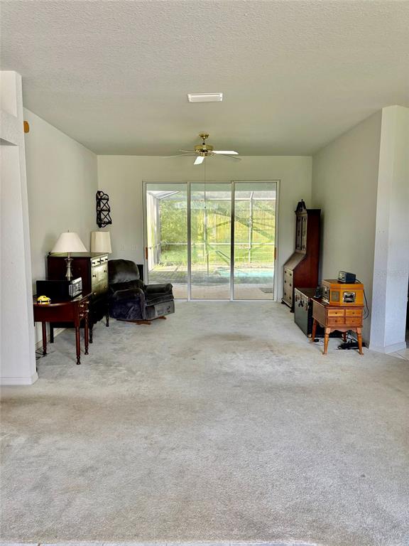A living room with carpeted flooring features a ceiling fan and sliding glass doors to a pool — 8680 SW 209TH COURT, DUNNELLON, FL