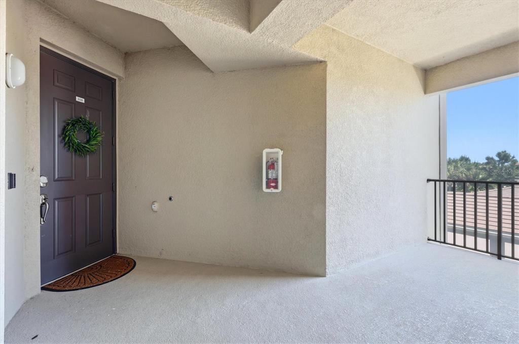 A dark brown front door with a wreath opens onto a covered concrete balcony — 17626 GAWTHROP DRIVE UNIT 208, BRADENTON, FL