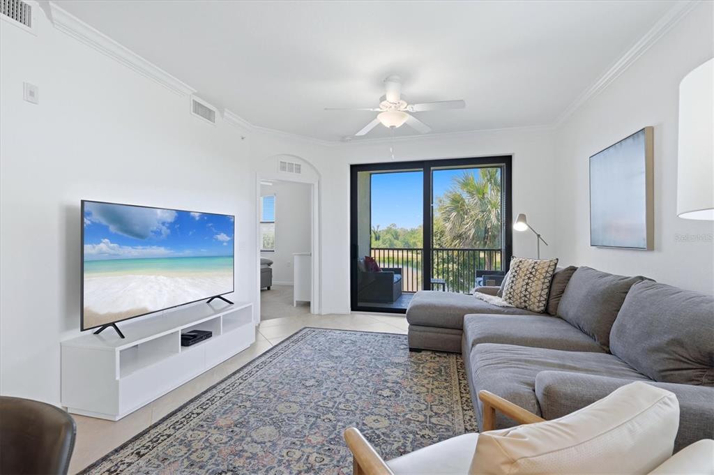 A living room features a grey sectional sofa, a television on a white stand, and balcony — 17626 GAWTHROP DRIVE UNIT 208, BRADENTON, FL