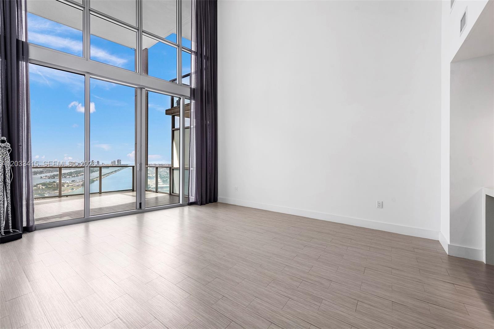 A bright, empty room features floor-to-ceiling windows, light wood flooring, and a balcony view — 1100 Biscayne Blvd # 5705, Miami FL 33132, MIAMI, FL