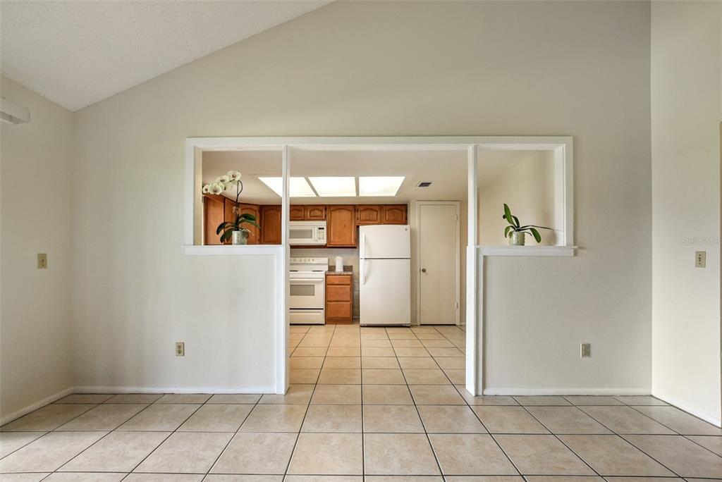 A view from a tiled room looking into a kitchen with wood cabinets and appliances — 309 REDWING WAY, CASSELBERRY, FL