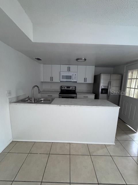 A kitchen features white cabinets, stainless steel appliances, a sink, and light-colored tile flooring — 4546 LIGHTHOUSE CIRCLE UNIT 14, ORLANDO, FL