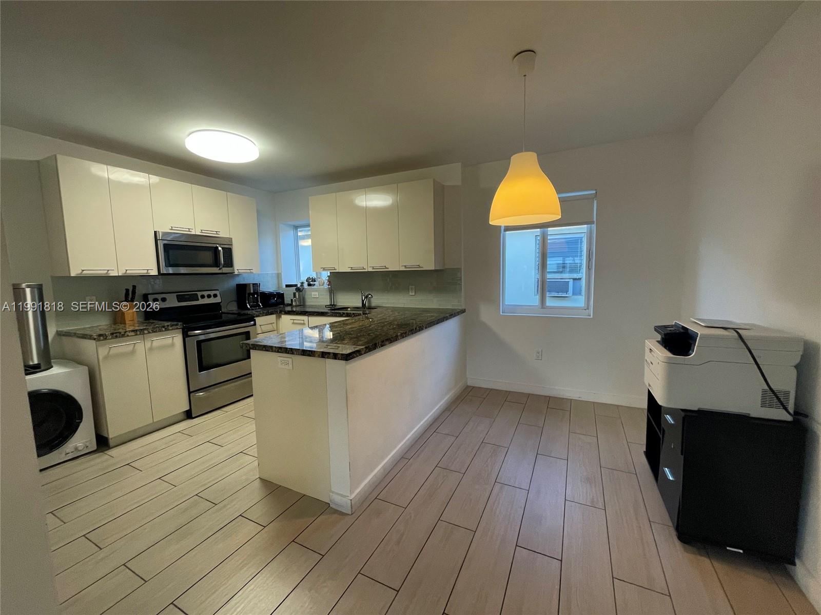 A kitchen features white cabinets, granite countertops, stainless steel appliances, and light wood-look tile flooring — 625 77th St # 2, Miami Beach FL 33141, MIAMI BEACH, FL