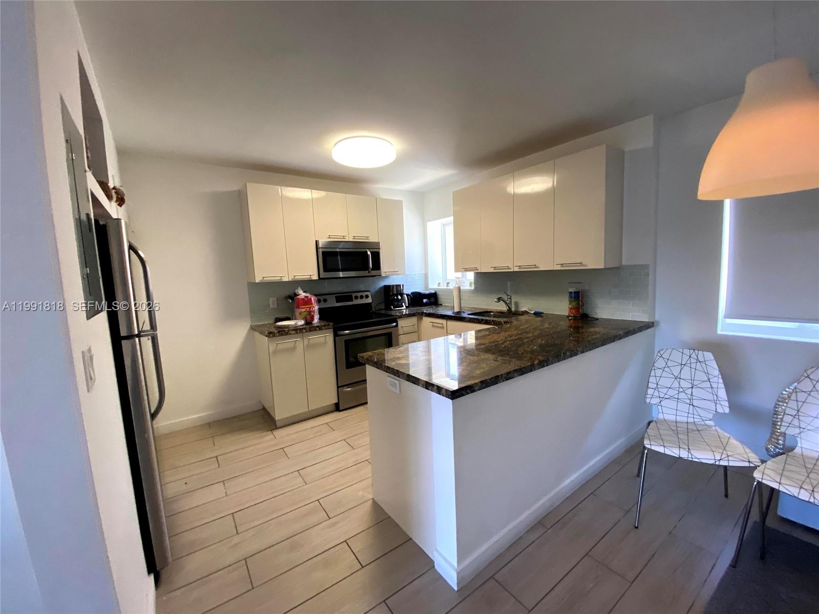 A kitchen features white cabinets, dark granite countertops, stainless steel appliances, and light tile flooring — 625 77th St # 2, Miami Beach FL 33141, MIAMI BEACH, FL