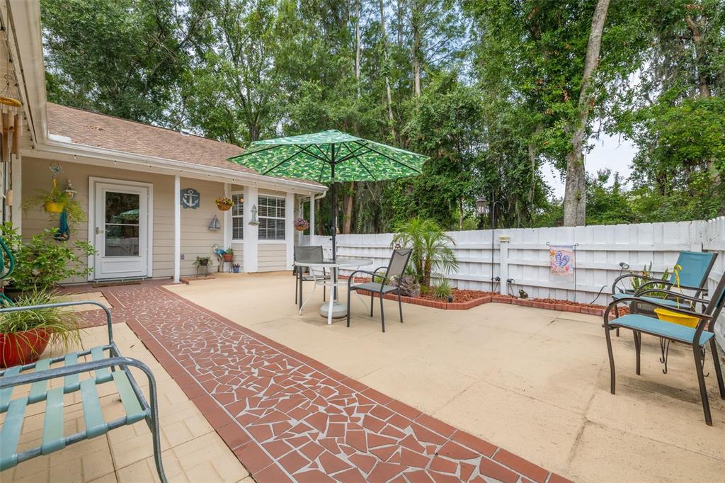 A backyard patio features a patterned walkway, a green umbrella, and outdoor furniture — 12432 KNOLLBROOK LANE, HUDSON, FL