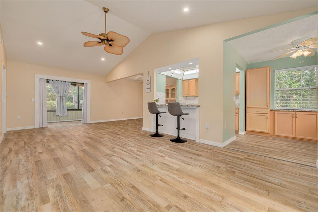 A living room with wood-look flooring, a vaulted ceiling, and a breakfast bar to the kitchen — 12432 KNOLLBROOK LANE, HUDSON, FL