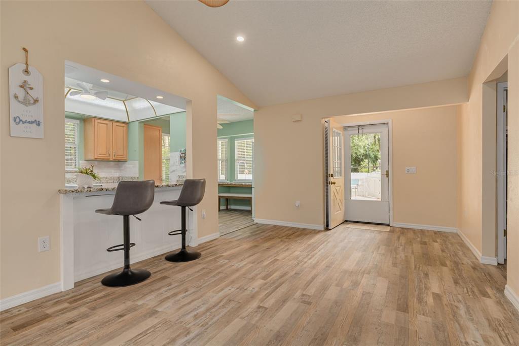 A dining area with wood-look flooring, a breakfast bar with two stools, and an exterior door — 12432 KNOLLBROOK LANE, HUDSON, FL