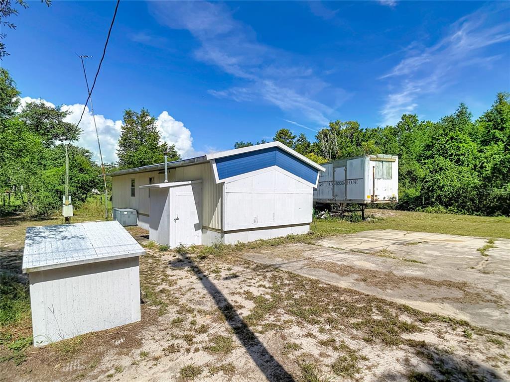 A mobile home with a small shed and a trailer parked on a grassy lot — 7848 NE 306TH COURT, FORT MC COY, FL