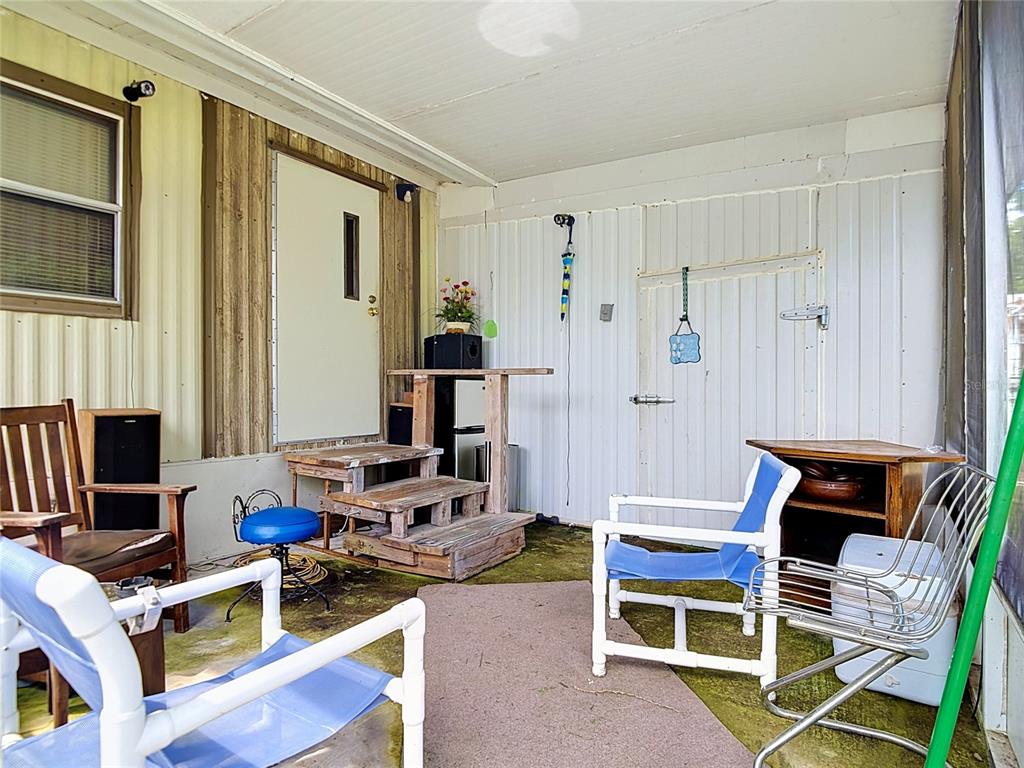 A covered porch features a white door, wooden steps, and several chairs on a concrete floor — 7848 NE 306TH COURT, FORT MC COY, FL