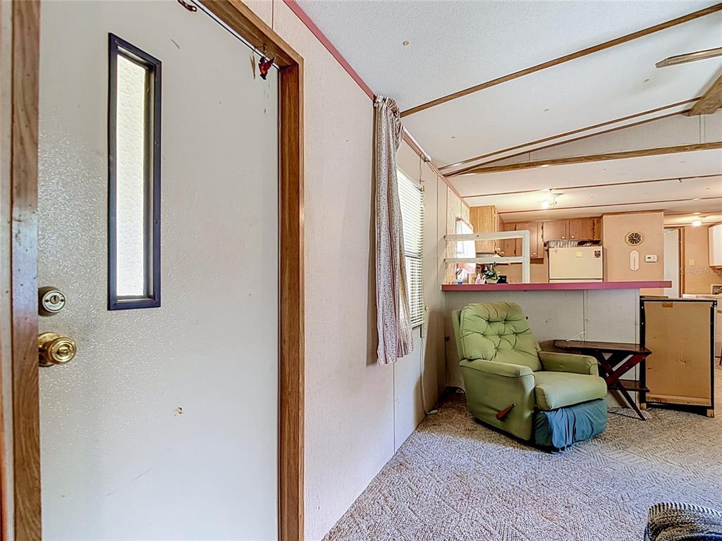 A living room with carpeted floors and a green recliner faces an open kitchen area — 7848 NE 306TH COURT, FORT MC COY, FL