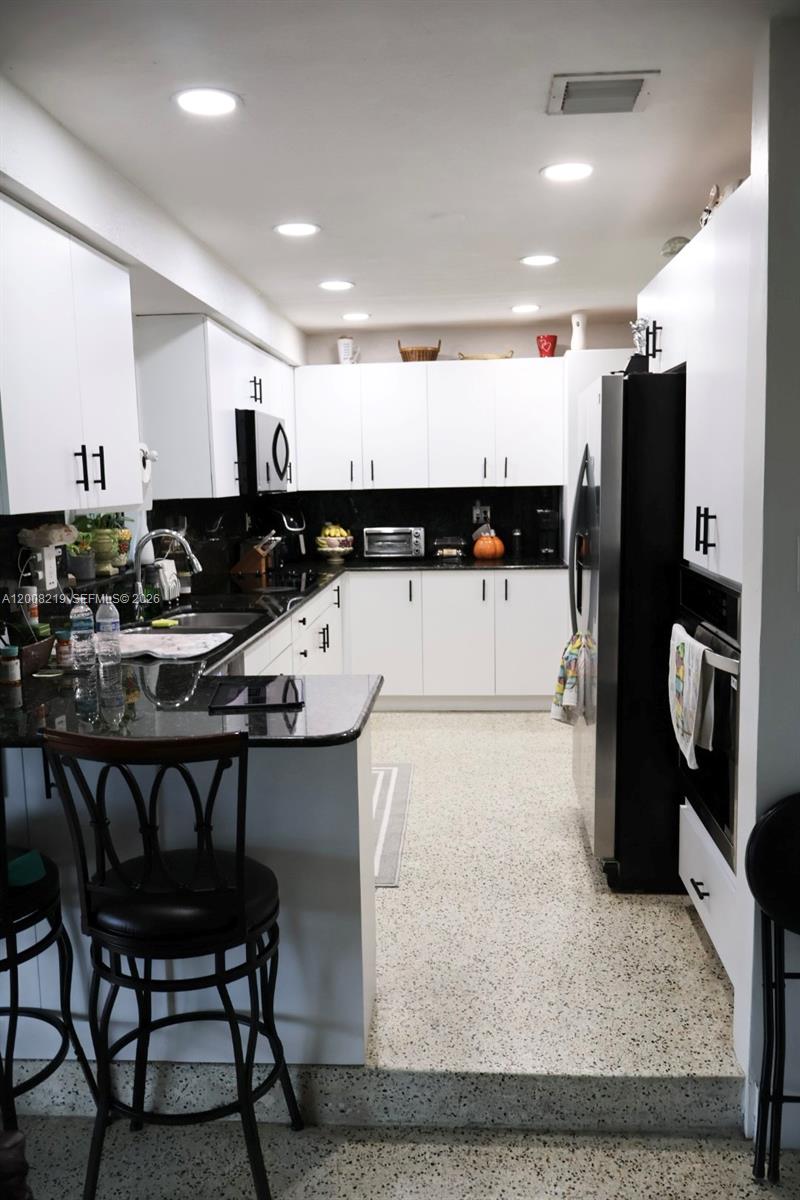 A kitchen features white cabinets, black countertops, stainless steel appliances, and a speckled floor — 11206 SW 1st St, Sweetwater FL 33174, SWEETWATER, FL