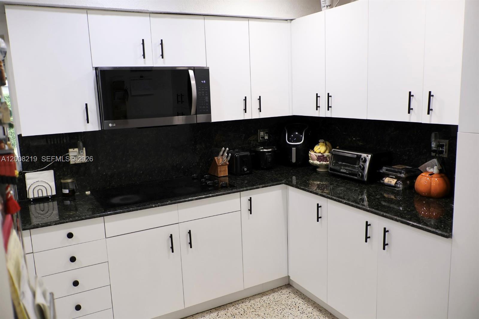 A kitchen features white cabinets, black countertops, and a built-in microwave above the stove — 11206 SW 1st St, Sweetwater FL 33174, SWEETWATER, FL