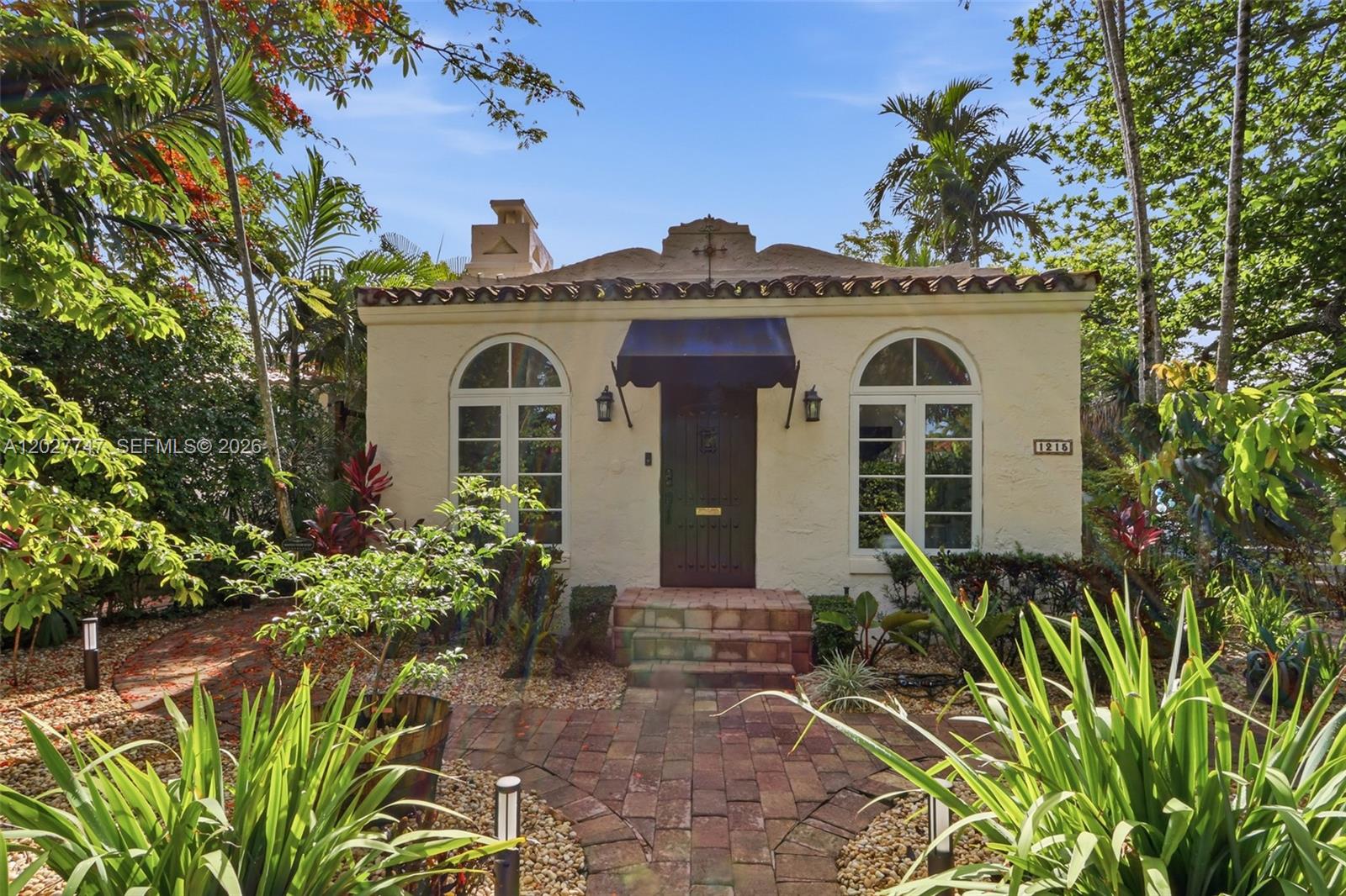 A single-story stucco house features a brick walkway, arched windows, and a dark awning — 1215 Madrid St, Coral Gables FL 33134, CORAL GABLES, FL