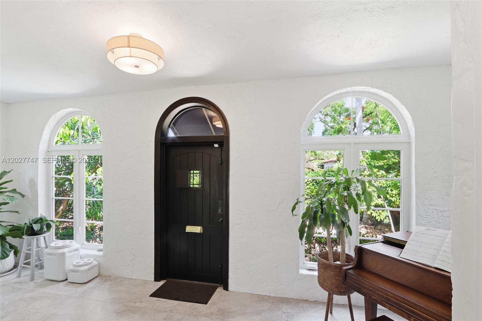 An entryway features a dark arched door, two arched windows, a piano, and white walls — 1215 Madrid St, Coral Gables FL 33134, CORAL GABLES, FL