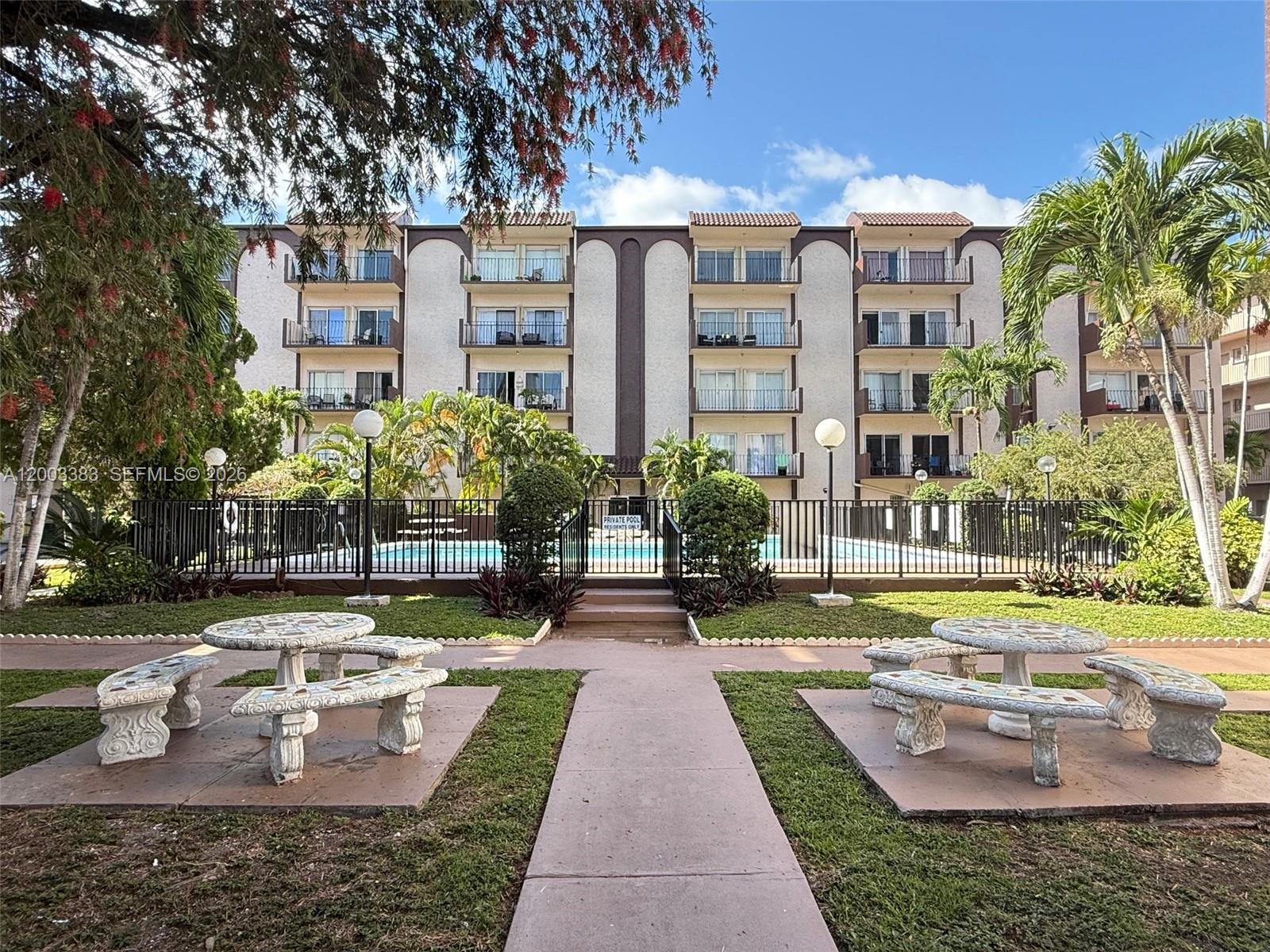 An exterior view of a multi-story apartment building with a swimming pool and stone benches — 1950 W 54th St # 115, Hialeah FL 33012, HIALEAH, FL