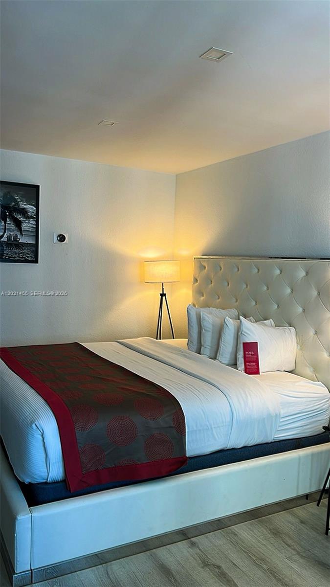 A bedroom features a tufted white headboard, a bed with a patterned runner, and a floor lamp — SUNNY ISLES BEACH, FL