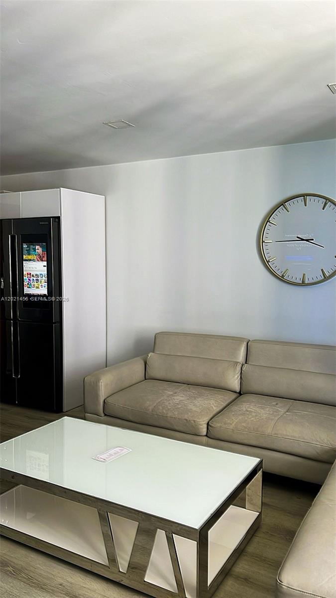 A living room features a beige sofa, a glass-topped coffee table, and a wall-mounted clock — SUNNY ISLES BEACH, FL