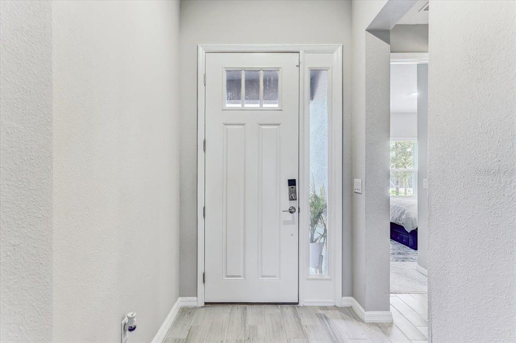 A white front door with a glass sidelight opens into a bright, neutral-toned entryway — 33886 LANDSMAN LOOP, WESLEY CHAPEL, FL