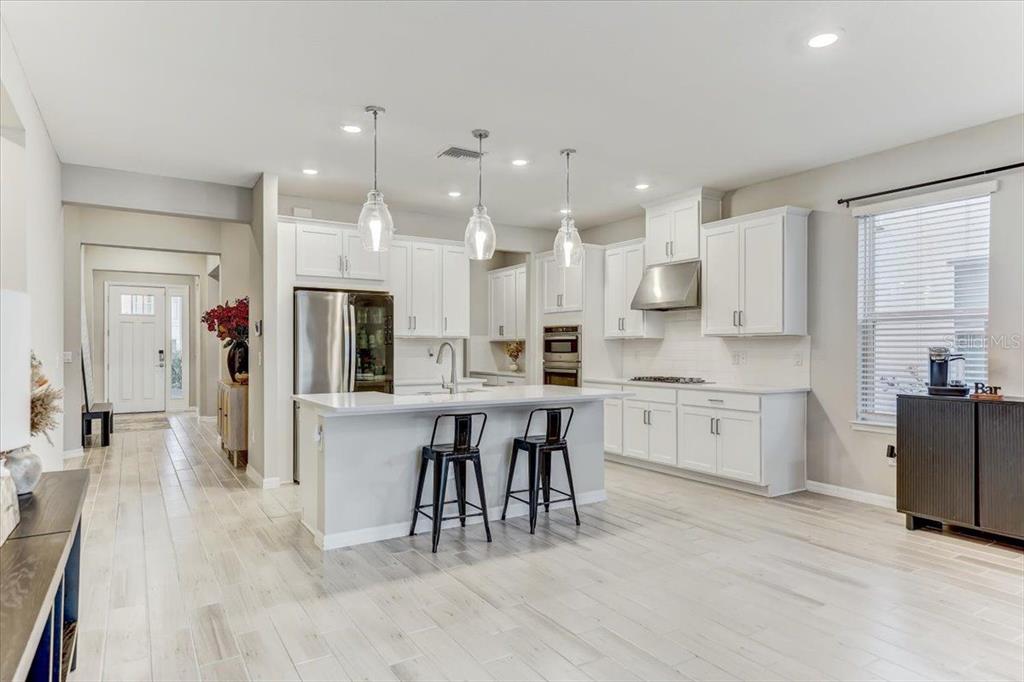 A modern kitchen features white cabinetry, a central island with bar stools, and light flooring — 33886 LANDSMAN LOOP, WESLEY CHAPEL, FL