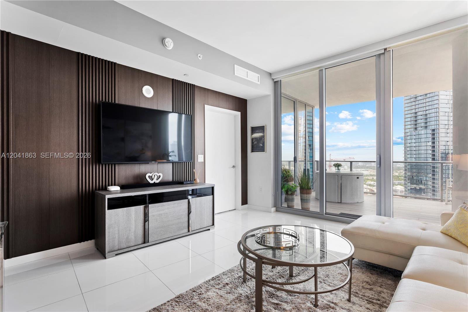A modern living room features a slatted wood accent wall, white tile floors, and balcony access — 851 NE 1st Ave # 3900, Miami FL 33132, MIAMI, FL
