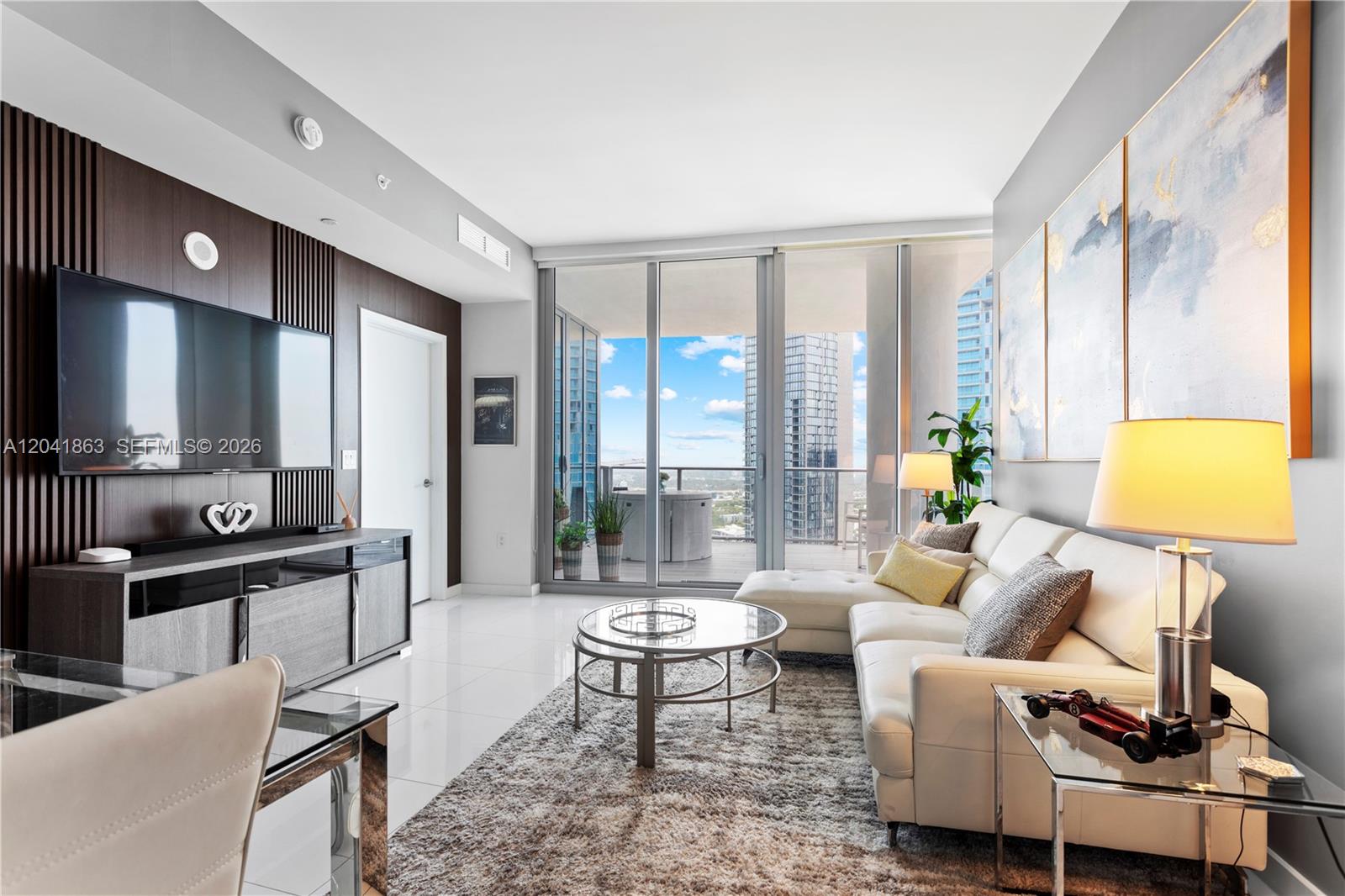 A modern living room features a white sectional sofa, glass coffee table, and balcony access — 851 NE 1st Ave # 3900, Miami FL 33132, MIAMI, FL