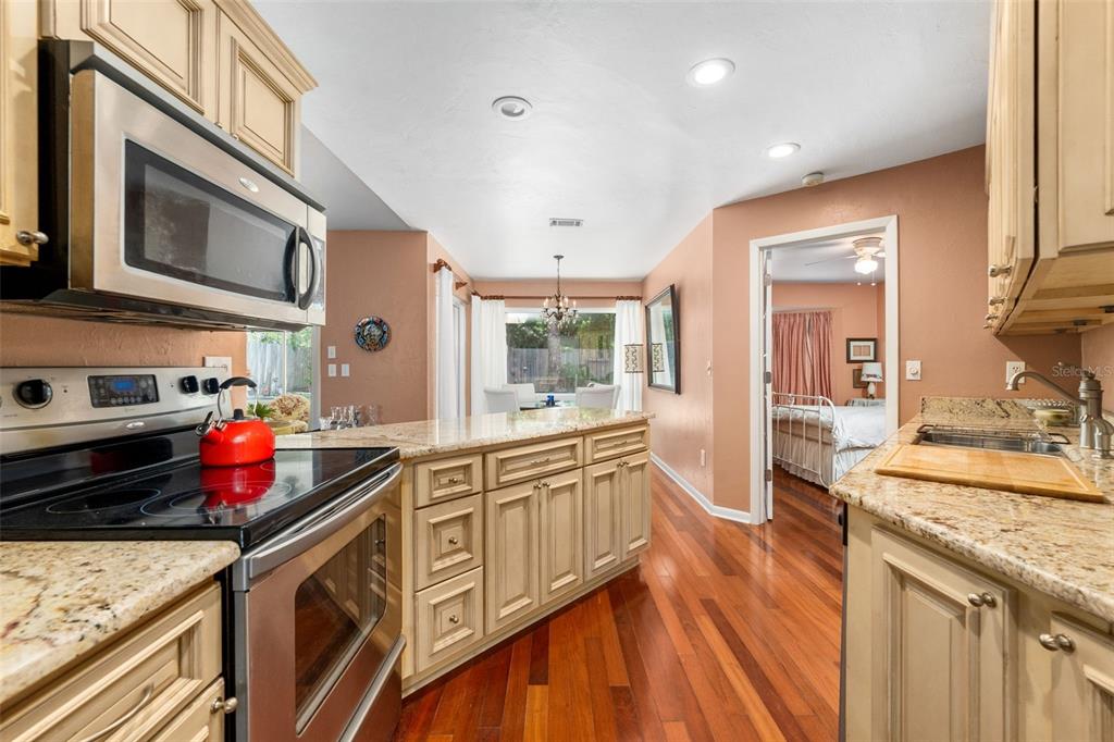 A kitchen with granite countertops, stainless steel appliances, and wood flooring leads to a dining area — 3815 NW 48TH TERRACE, GAINESVILLE, FL
