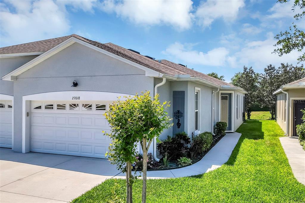 A single-story house with a white garage, gray stucco exterior, and a small front garden — 27018 WHITE PLAINS WAY, LEESBURG, FL