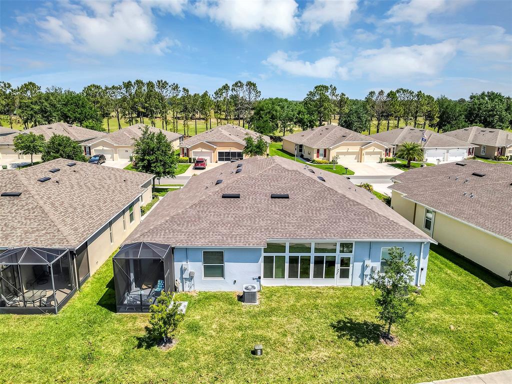 An aerial view of a suburban house with a screened-in patio and a grassy backyard — 27018 WHITE PLAINS WAY, LEESBURG, FL