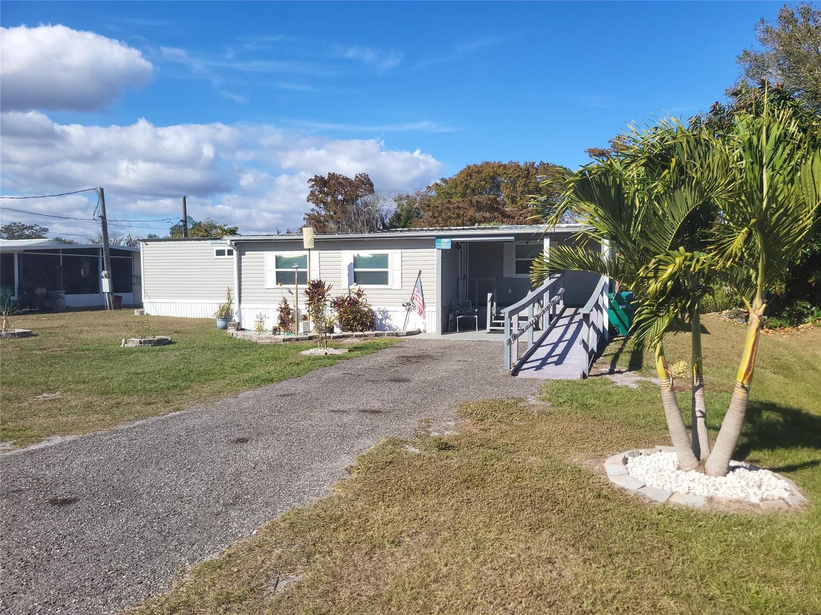 A single-story manufactured home with a gravel driveway, a wheelchair ramp, and a palm tree — 4037 SE 27th Street, Okeechobee FL 34974, OKEECHOBEE, FL