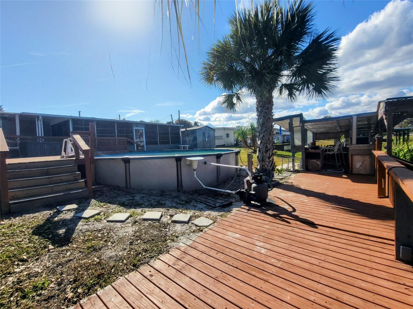 An above-ground swimming pool sits in a yard next to a wooden deck and palm tree — 4037 SE 27th Street, Okeechobee FL 34974, OKEECHOBEE, FL