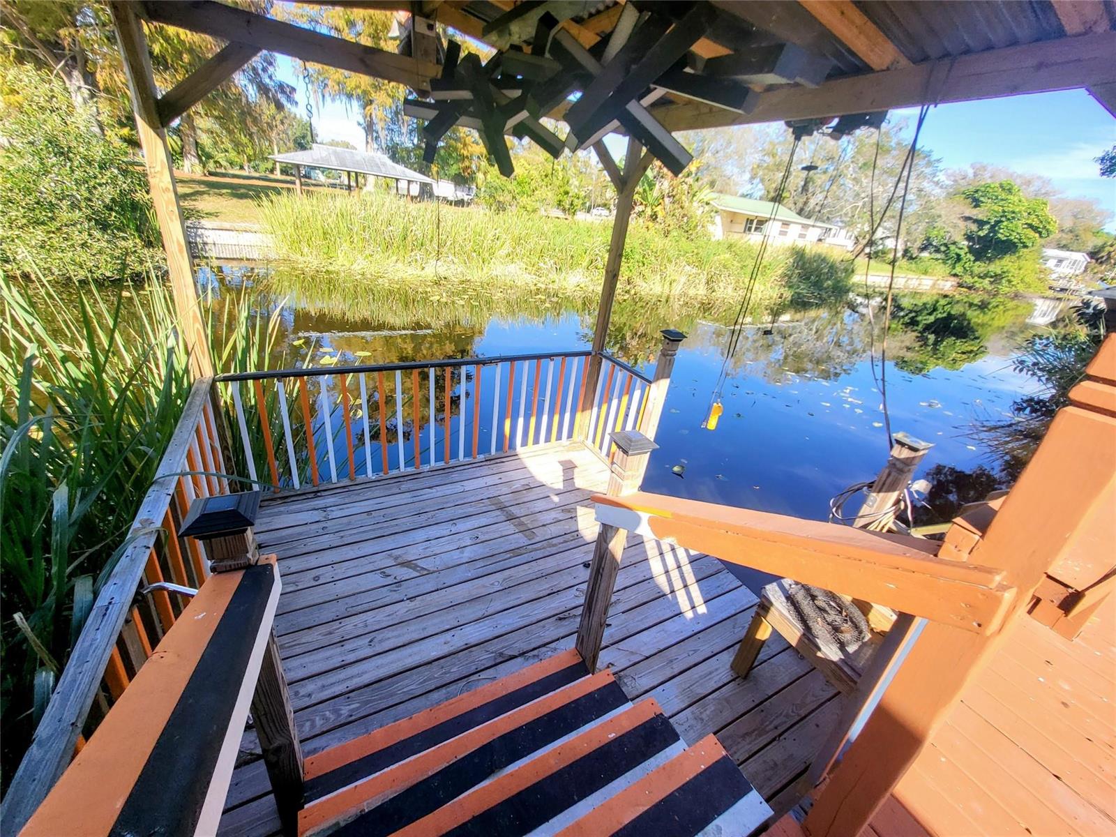 A wooden deck with a covered roof overlooks a pond surrounded by tall green reeds — 4037 SE 27th Street, Okeechobee FL 34974, OKEECHOBEE, FL