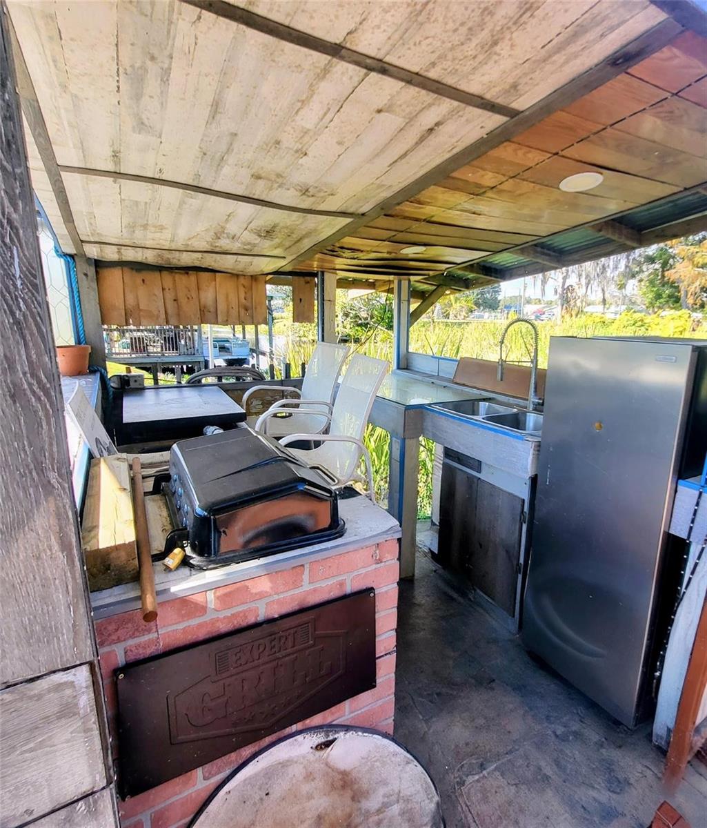 An outdoor kitchen features a grill, sink, refrigerator, and seating under a wooden roof — 4037 SE 27th Street, Okeechobee FL 34974, OKEECHOBEE, FL