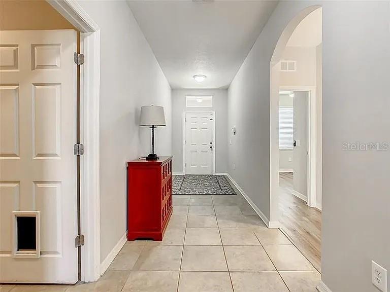 A tiled entryway features a red cabinet, a lamp, and an arched doorway leading inside — 210 BLACKSTONE CREEK ROAD, GROVELAND, FL