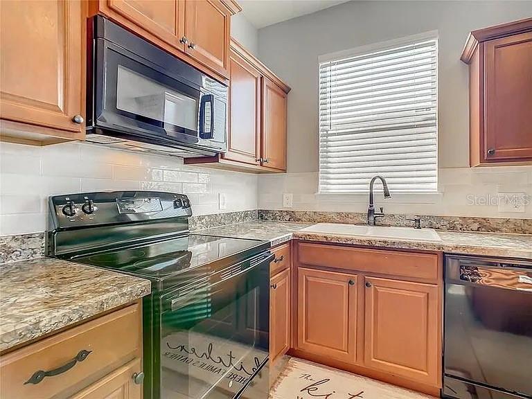 A kitchen features wood cabinets, a black microwave, a black stove, and a window — 210 BLACKSTONE CREEK ROAD, GROVELAND, FL