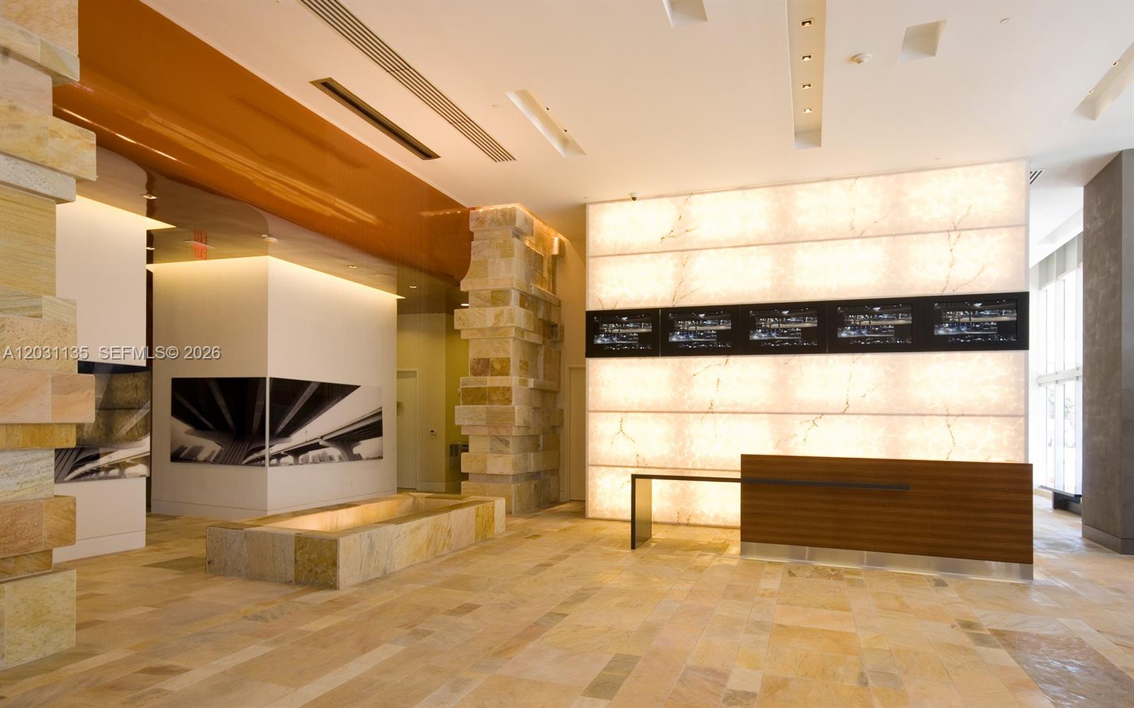 A modern lobby features a stone reception desk, backlit marble wall, and polished tile flooring — 500 Brickell Ave # 1808, Miami FL 33131, MIAMI, FL
