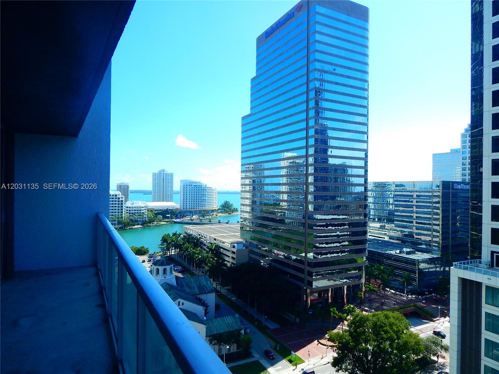 A high-rise balcony overlooks a city skyline, a body of water, and modern office buildings — 500 Brickell Ave # 1808, Miami FL 33131, MIAMI, FL
