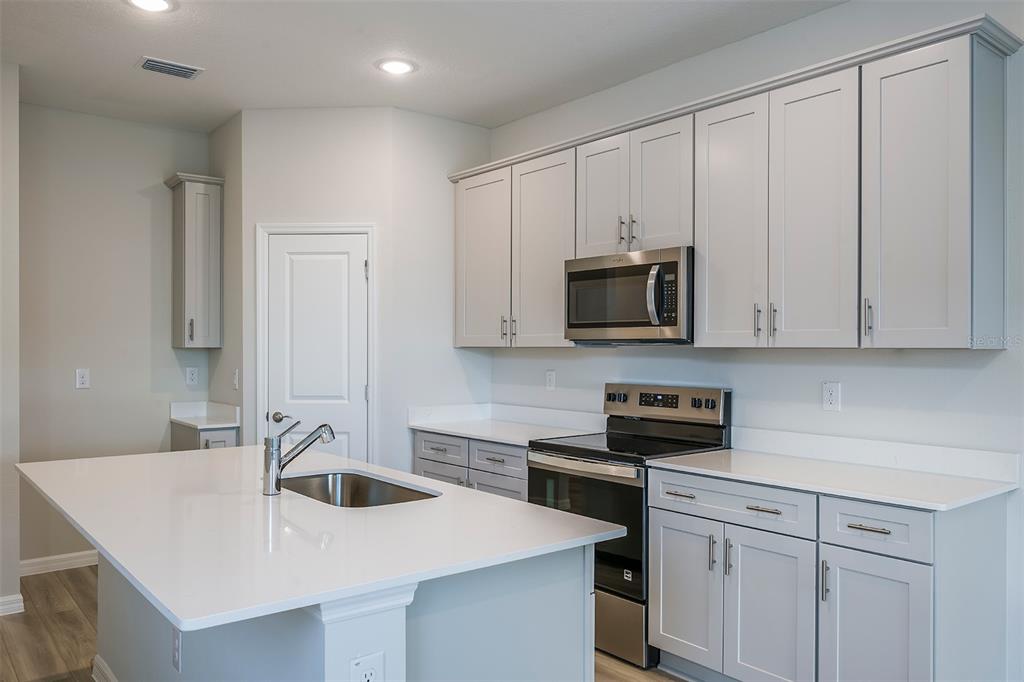 A kitchen features light gray cabinets, white countertops, a central island, and stainless steel appliances — 6125 SW 96TH PLACE, OCALA, FL