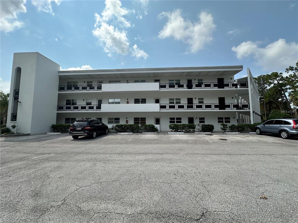 A three-story apartment building with exterior walkways and a parking lot in the foreground — 100 EL CAMINO DR UNIT 104, WINTER HAVEN, FL